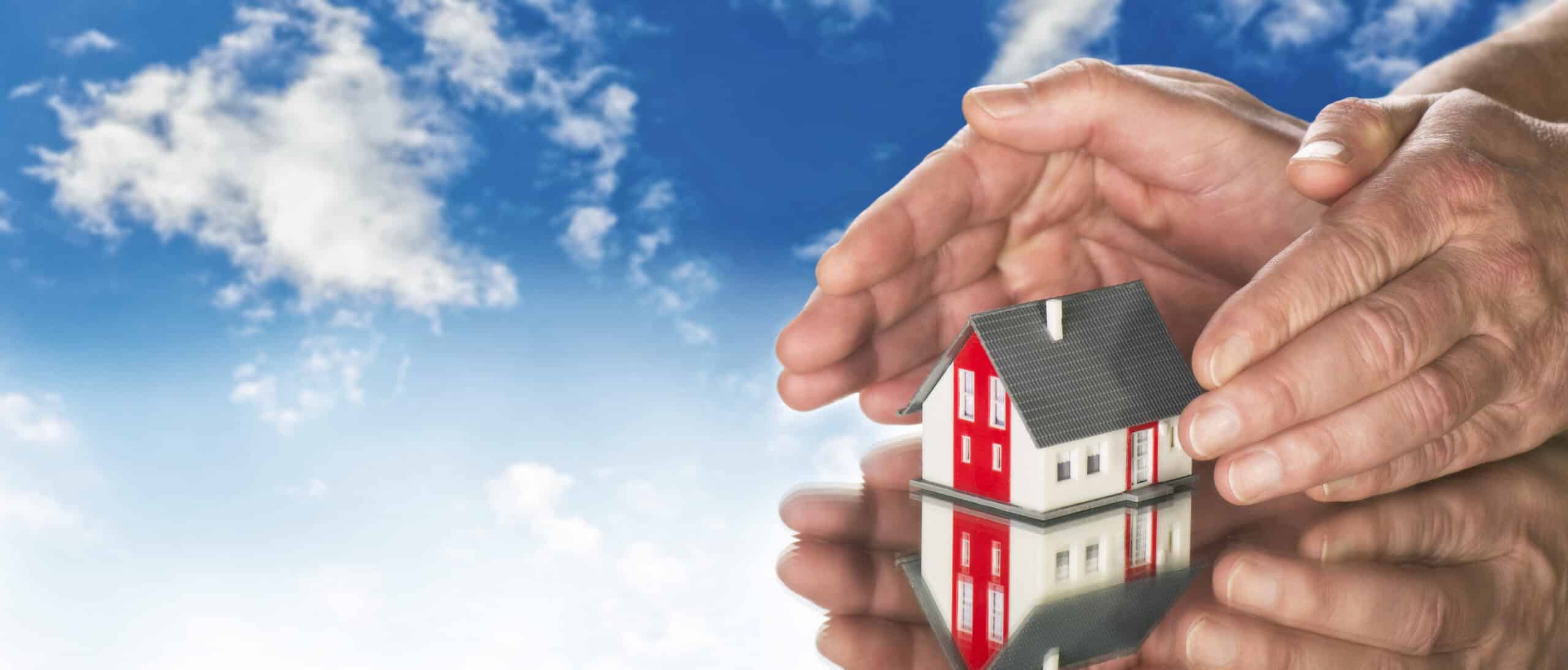 Hände legen sich schützend um ein Haus